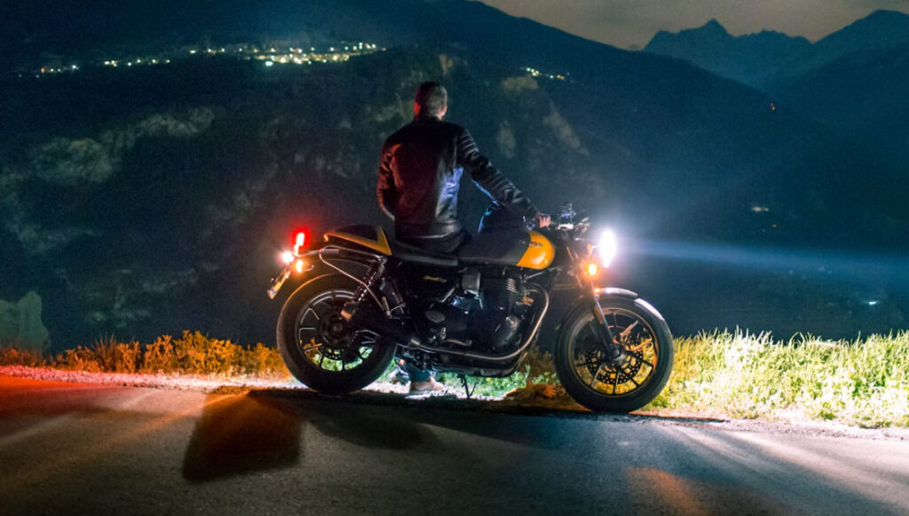 Motorrijder staat 's avonds naast zijn motor met verlichte koplampen